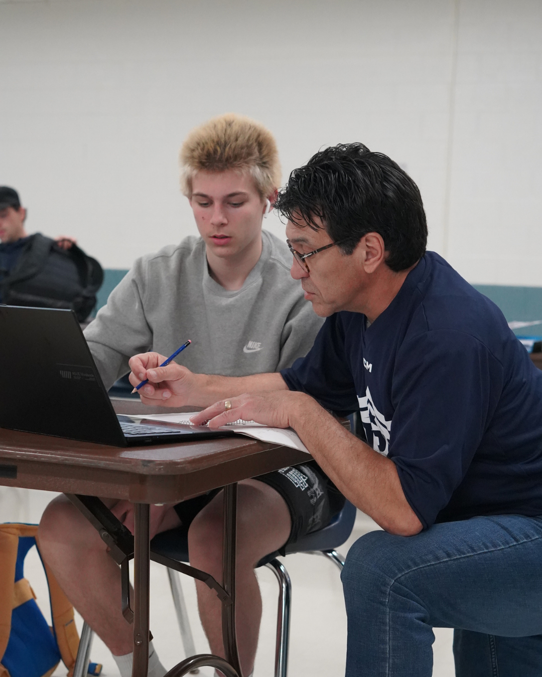 Teacher kneeling next to student's desk to work through an assignment with them.